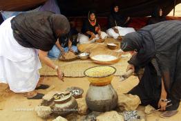 Image du Maroc Professionnelle de  Sous une tente bédouine plusieurs femmes du Sahara  préparent le couscous durant le grand Moussem de Tan Tan, classé en 2005 patrimoine immatériel humain mondial de l'Unesco. Le Moussem est une sorte de foire annuelle, à la fois économique, culturelle et sociale. Chaque année la majorité des tribus et des grandes familles nomades du désert se retrouvent sur un site désertique "Place de la Tolérance et de la Paix " à la périphérie de Tan Tan où  danse, chants, course de chameaux et fantasia font partie des festivités. , Samedi 18 septembre 2004, ((Photo / Abdeljalil Bounhar) 